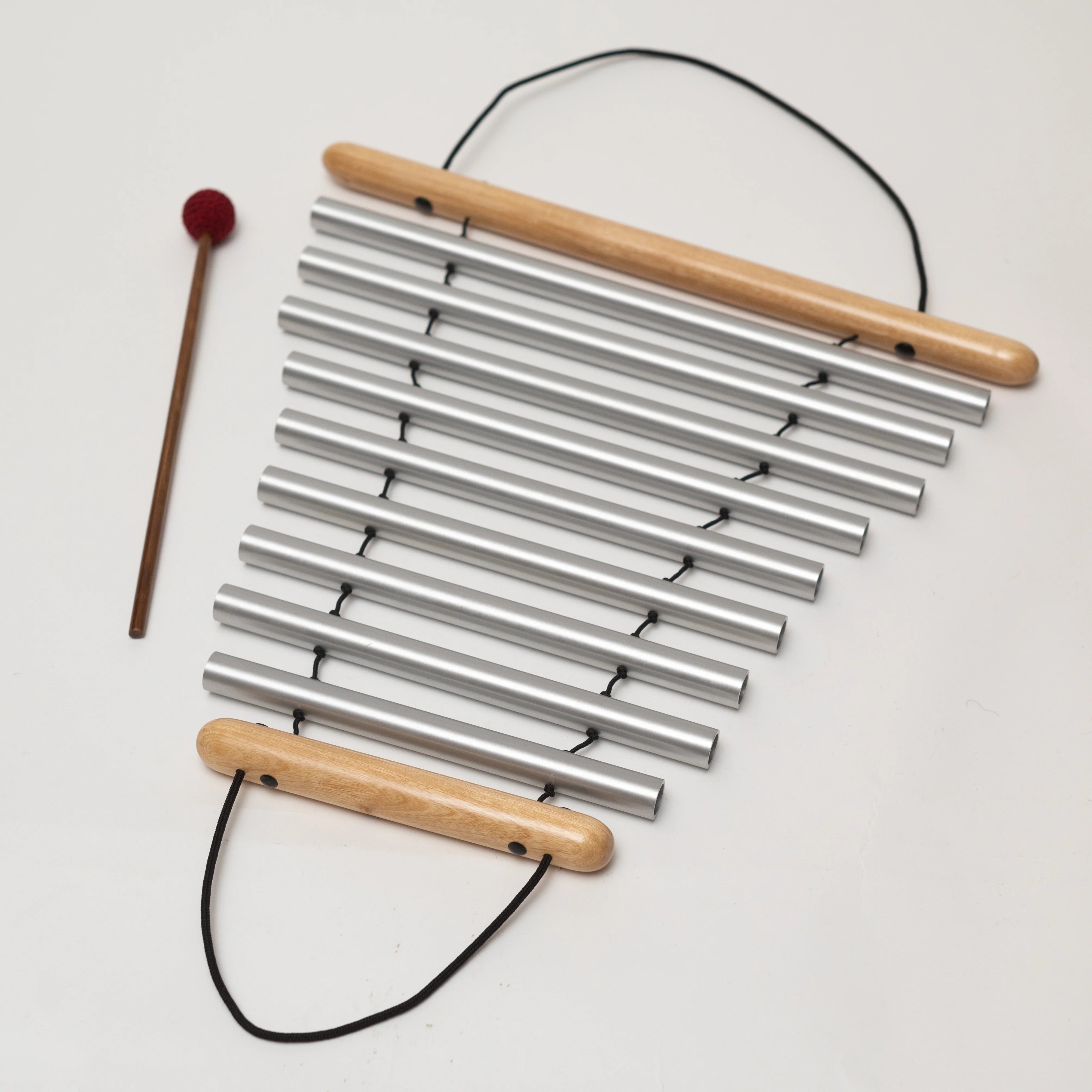 Metal chimes with wooden handles and a mallet on a light background
