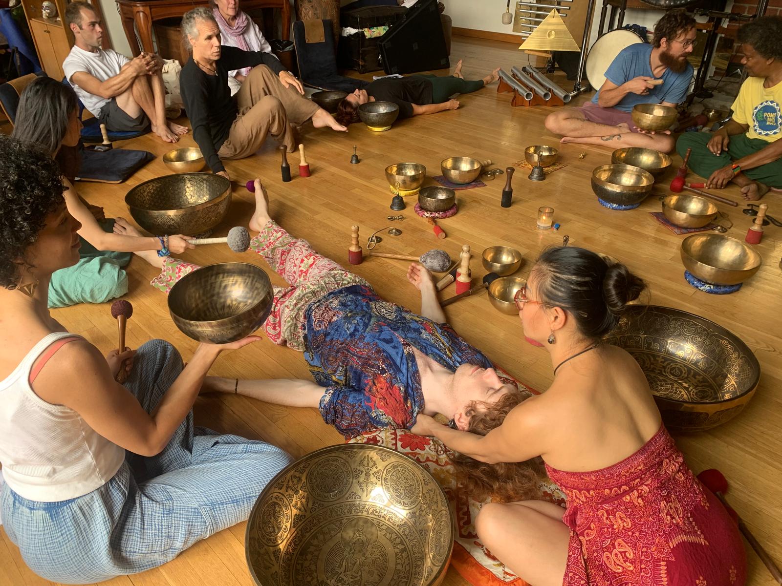 Group of people participating in a sound bath session with large metal bowls on a wooden floor.